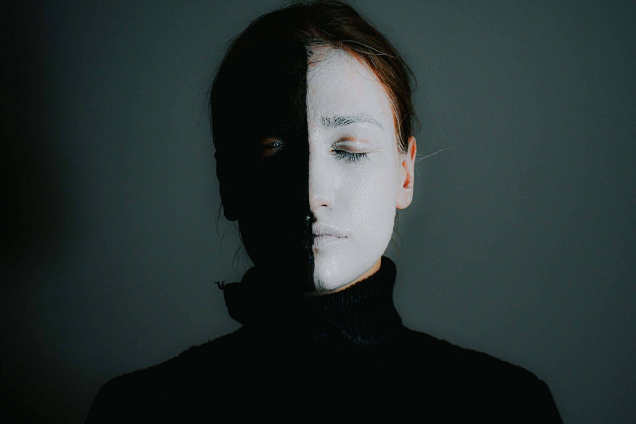 A person with their face painted black on one half and white on the other, eyes closed