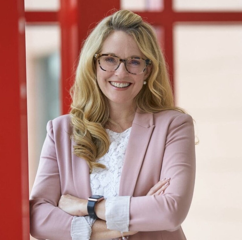 Dr. Erica Sirrine, a smiling woman with glasses and long blond hair in a pink jacket with arms crossed