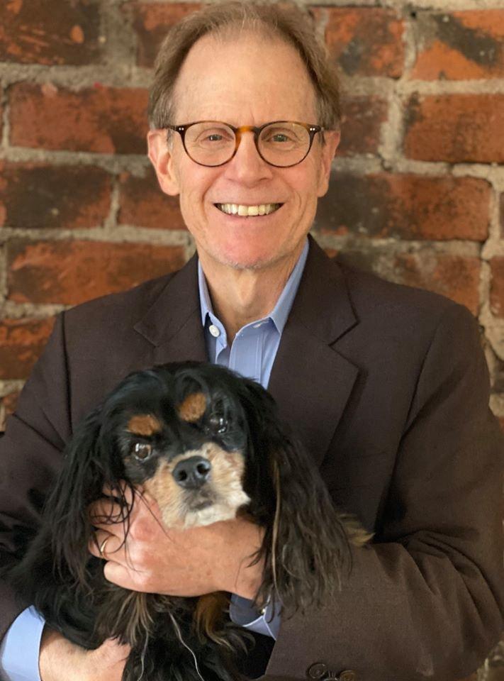 Dr. Dan Siegel, a smiling older man in a suit with glasses, red hair, and holding his dog
